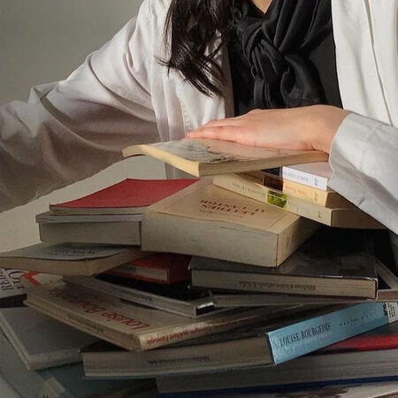 A person with a hand lying on a messy stack of books
